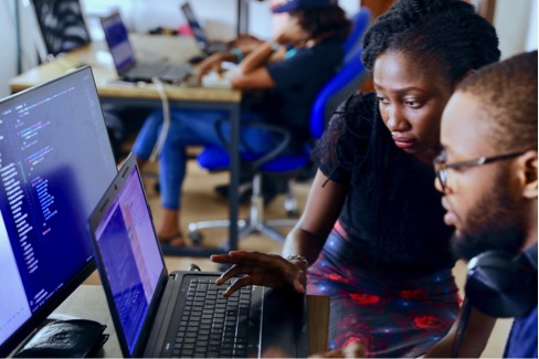 A woman and man are looking at a laptop, which is displaying code