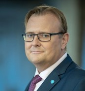 Jaroslaw Ponder, white male with light short light hair and glasses, wearing a navy suit and ITU pin 