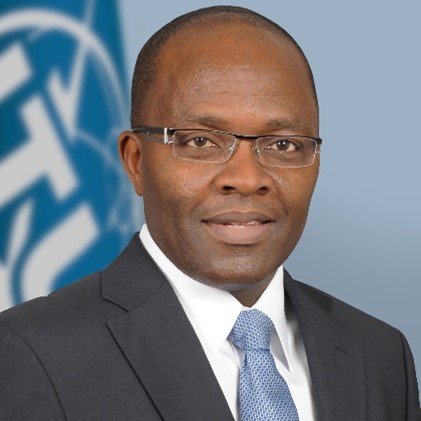 Cosmas Luckyson Zavazava, black male wearing glasses, a dark suit, and blue tie in front of the ITU flag.